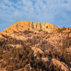 Sunlit Horsetooth Mountain with rugged terrain in Fort Collins, Colorado, against a clear sky at dusk.