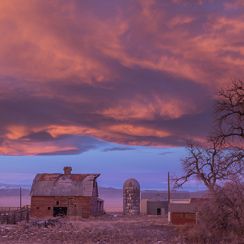 Historic farm structures under a dramatic purple sunset sky in Johnstown, Colorado